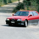 Red Alfa Romeo 164 being driven along a dusty track