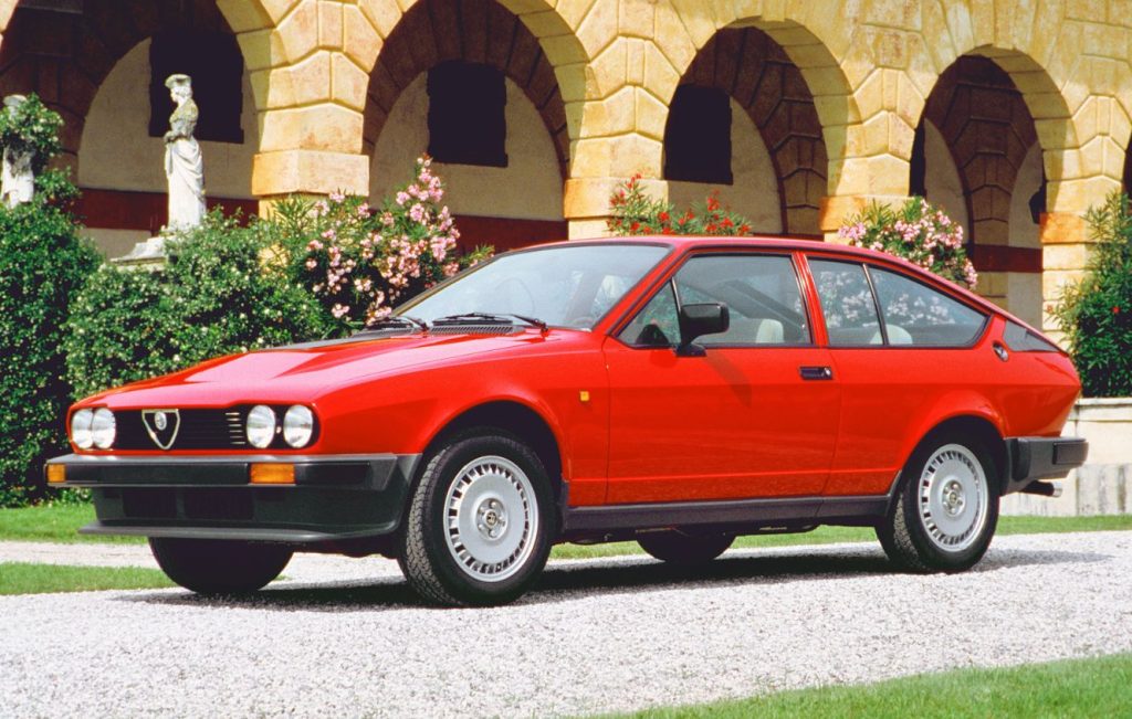 Red Alfa Romeo GTV parked in front of a stone building