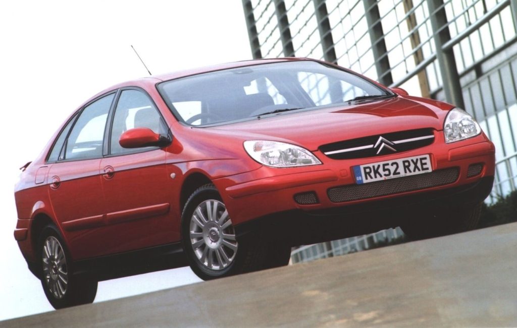 Metallic red Citroen C5 parked next to a metal fence