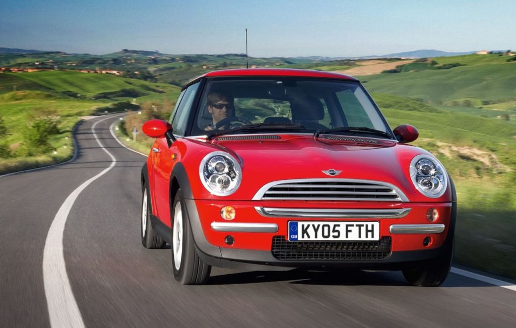 Man driving a red Mini One along a road through hills
