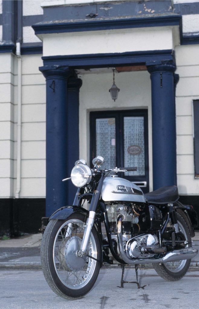 Norton Dominator 88 motorcycle parked outside a blue and white building