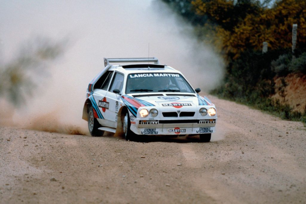 Lancia Delta S4 in Martini livery powering through a dusty gravel stage on the Group B rally circuit