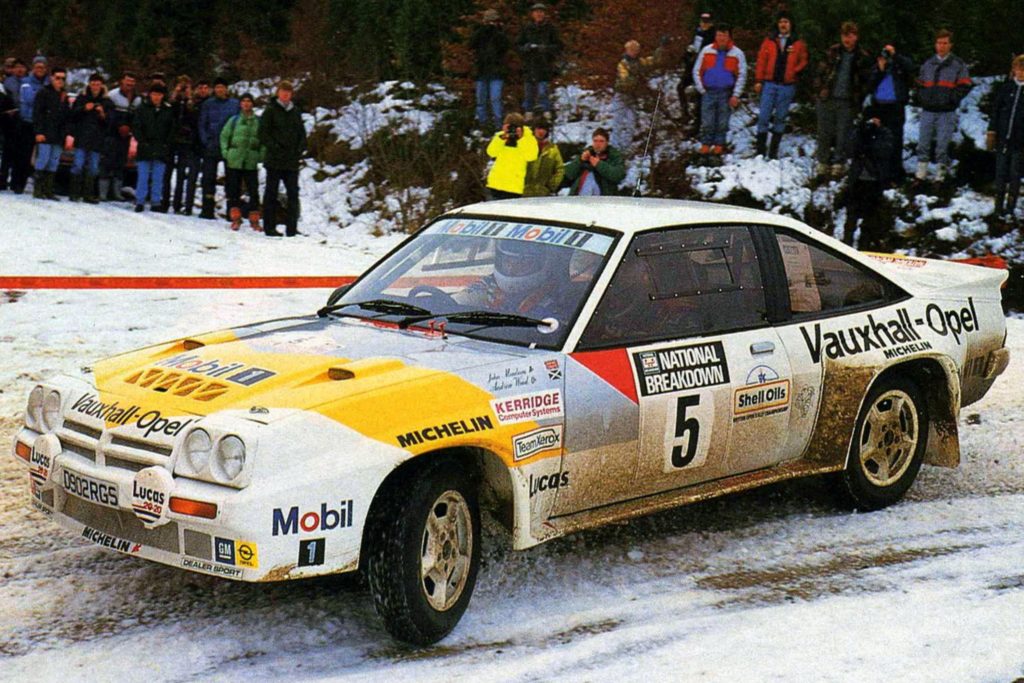 Vauxhall-Opel Manta B400 Group B rally car in yellow and white livery cornering on a snowy stage with spectators lining the road