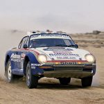 Rothmans-liveried Porsche 959 Group B car racing through desert sand dunes on the Paris-Dakar rally