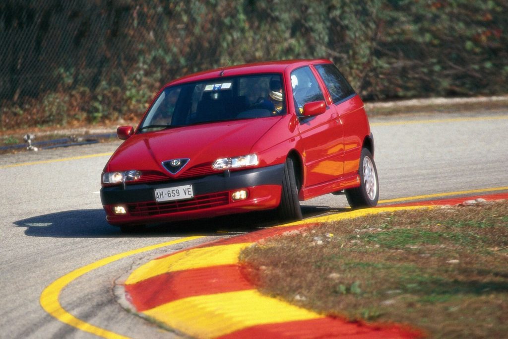 Red Alfa Romeo 145 Quadrifoglio three-door hatchback being driven on a race circuit with kerbs visible in the foreground