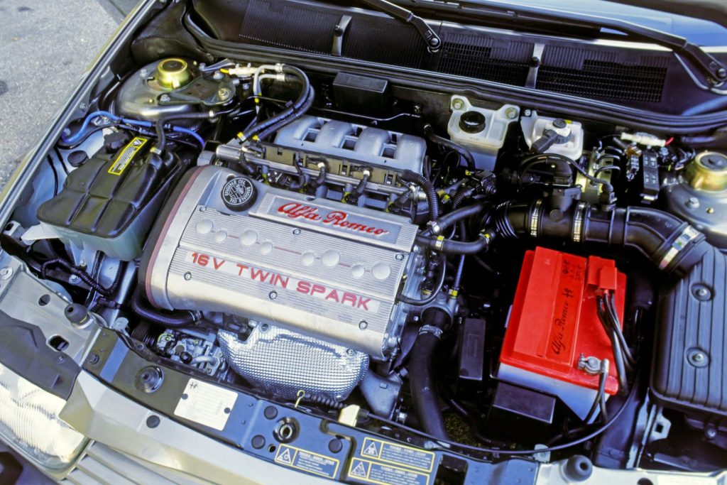 Alfa Romeo 16V Twin Spark engine bay with red Alfa Romeo branded battery cover and silver cam cover