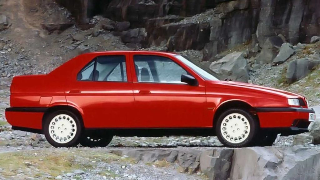 Red Alfa Romeo 155 saloon parked on gravel in front of a stone track