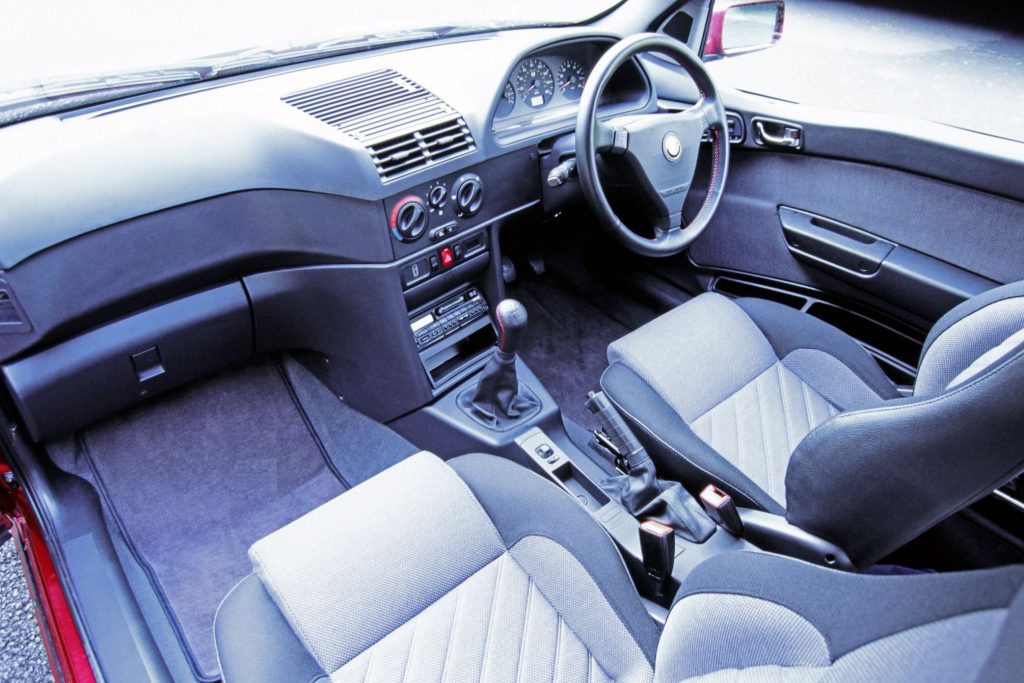 Alfa Romeo 145 interior showing grey two-tone front seats, dashboard, steering wheel and manual gearshift from the passenger side