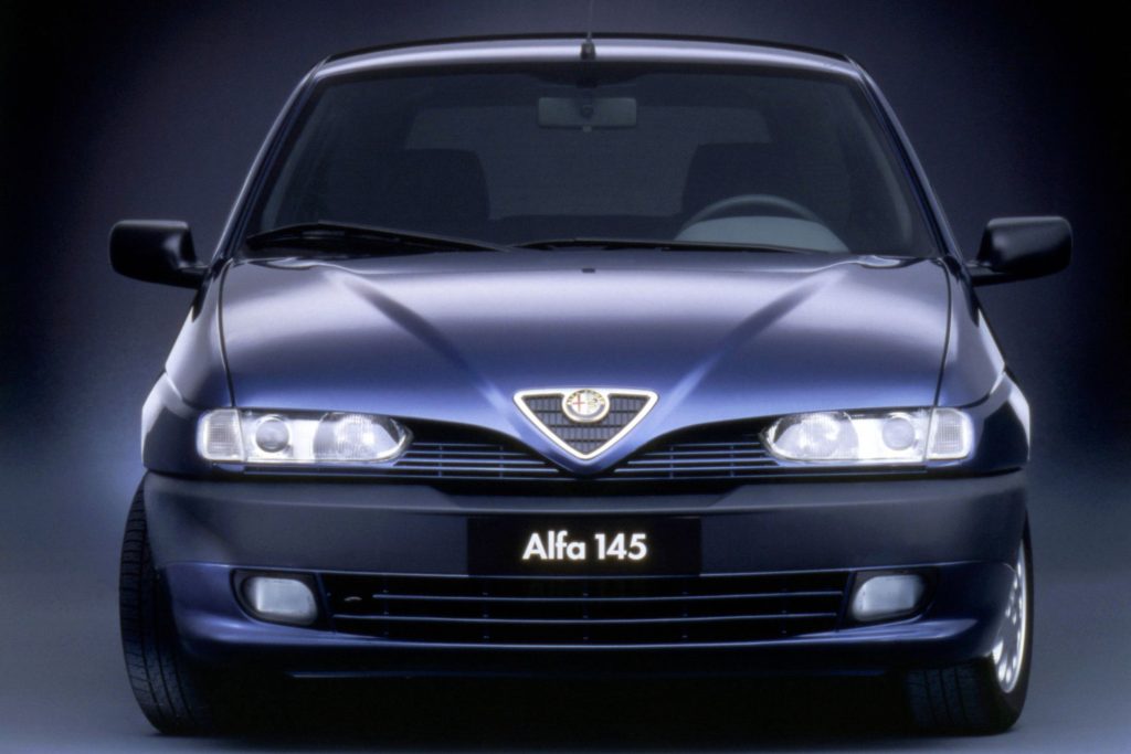 Front-on studio press photo of a dark blue Alfa Romeo 145 showing the Alfa Romeo badge, twin headlights and front grille