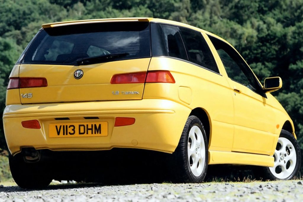 Rear three-quarter view of a yellow Alfa Romeo 145 1.8 Twin Spark three-door hatchback parked on gravel in front of trees