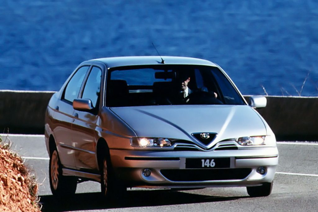 Silver Alfa Romeo 146 saloon being driven on a coastal road with blue sea visible in the background