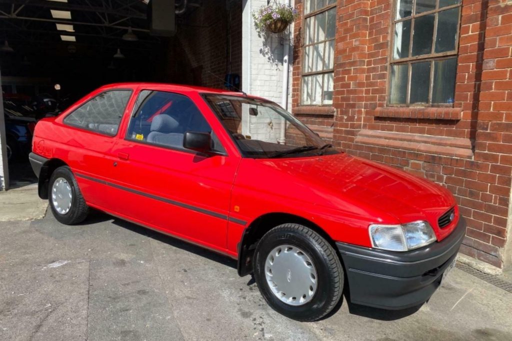 Red Mk4 Ford Escort three-door hatchback parked outside a red brick building next to a garage entrance