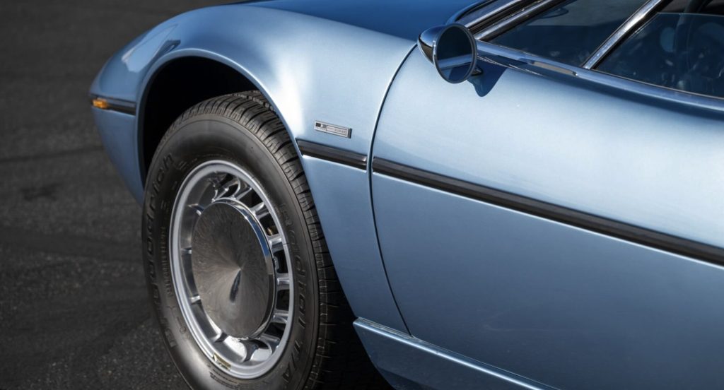 Front wheel arch and fender detail of a light blue Maserati Bora, showing the BFGoodrich radial tire on a multi-spoke alloy wheel