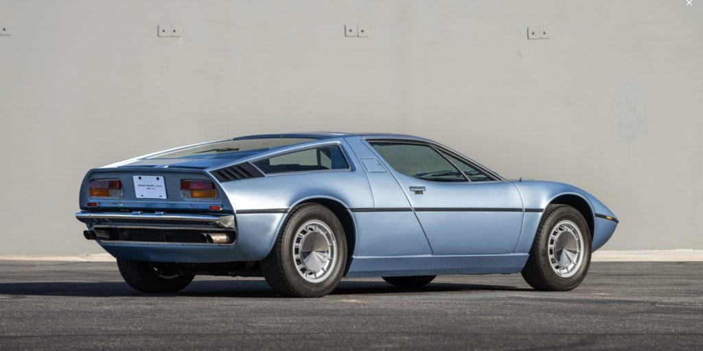 Rear three-quarter view of a light blue Maserati Bora with a Broad Arrow Auctions placard
