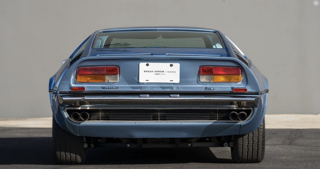 Straight-on rear view of a light blue Maserati Bora with a Broad Arrow Auctions placard, showing the full-width tail with quad rectangular taillights, "Maserati" and "Bora" lettering, and quad exhaust pipes.