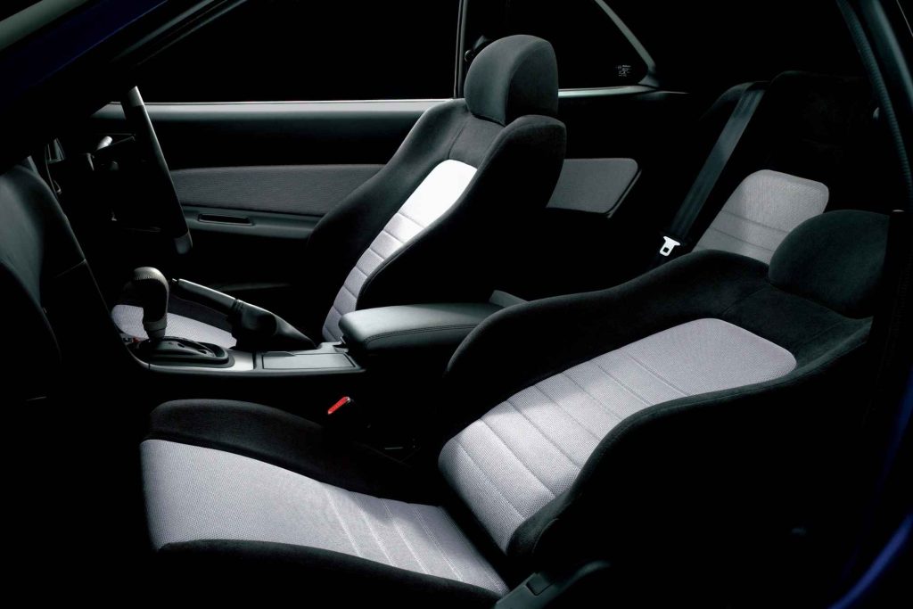 Black and gray two-tone fabric sport seats in the interior of a Nissan Skyline R34, with center console and automatic gear shifter visible