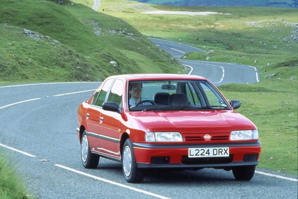 Red Nissan Primera P10 four-door saloon on a winding Scottish highland road, front view