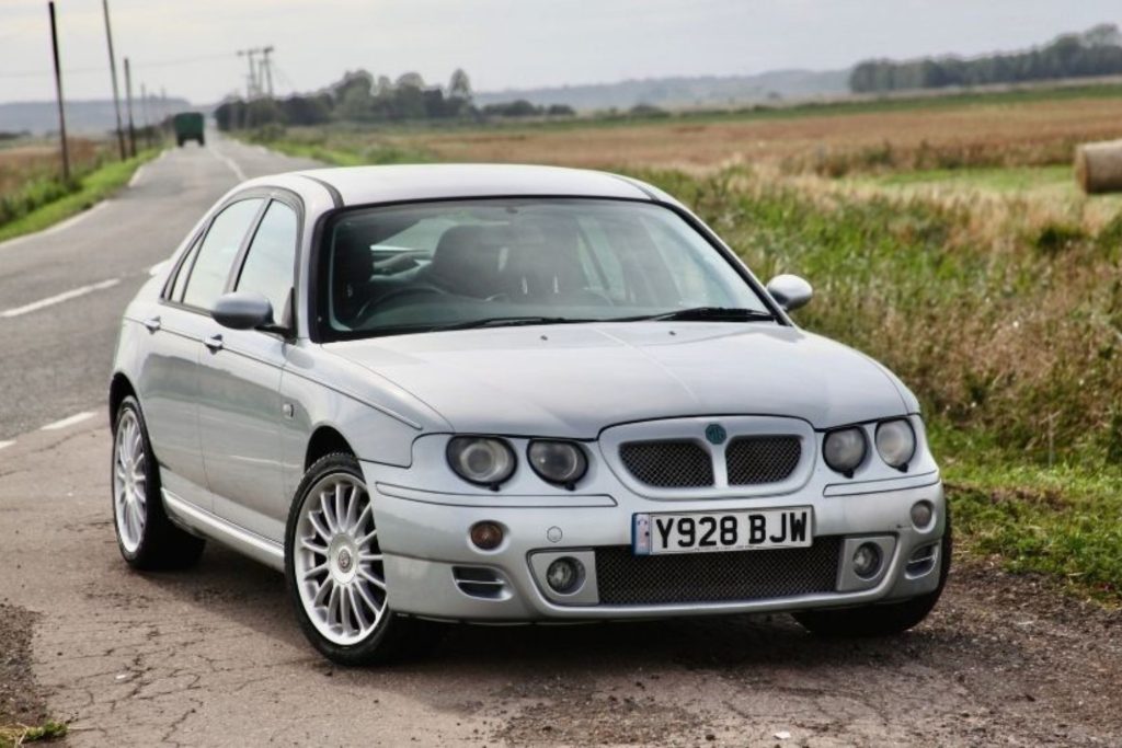 Silver MG ZT V6 saloon parked on a rural road with fields and open countryside in the background