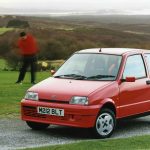 Red Fiat Cinquecento Sporting parked on a golf course with a golfer and Titleist bag visible in the background