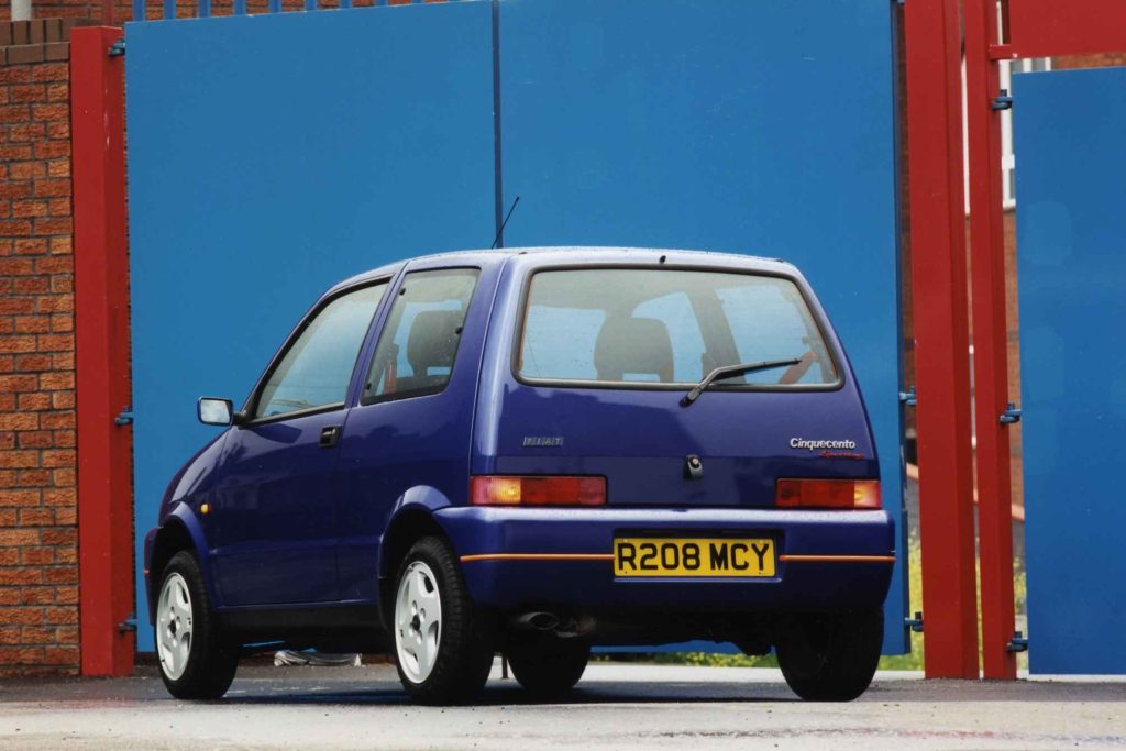 Blue Fiat Cinquecento Sporting rear three-quarter view parked between blue and red industrial gates
