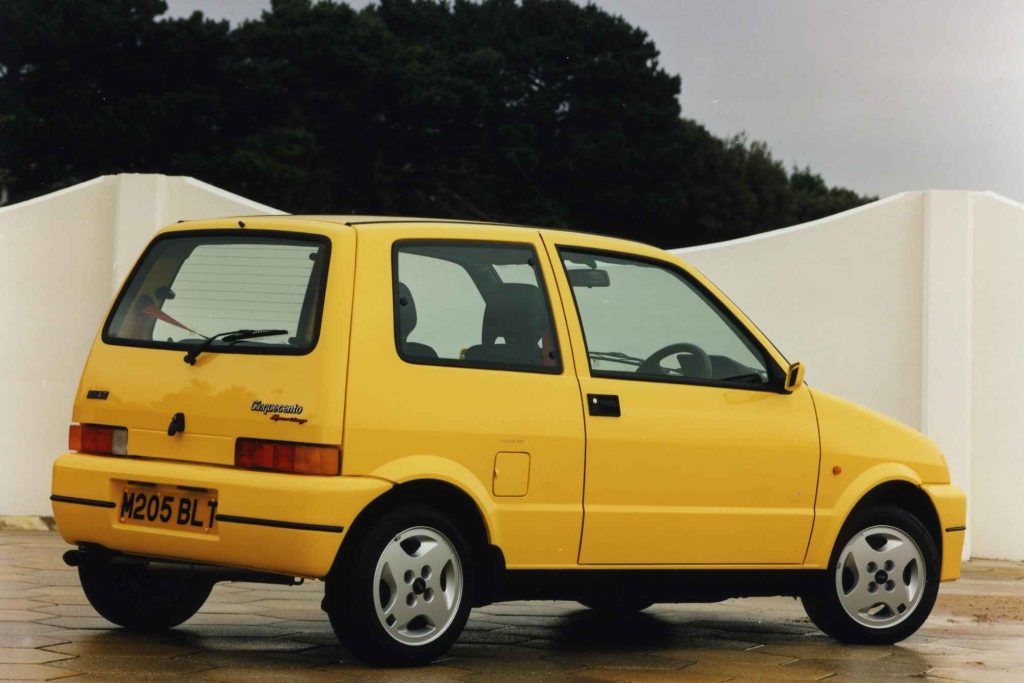 Yellow Fiat Cinquecento Sporting rear three-quarter view parked against a white wall, showing the Cinquecento Sporting badge