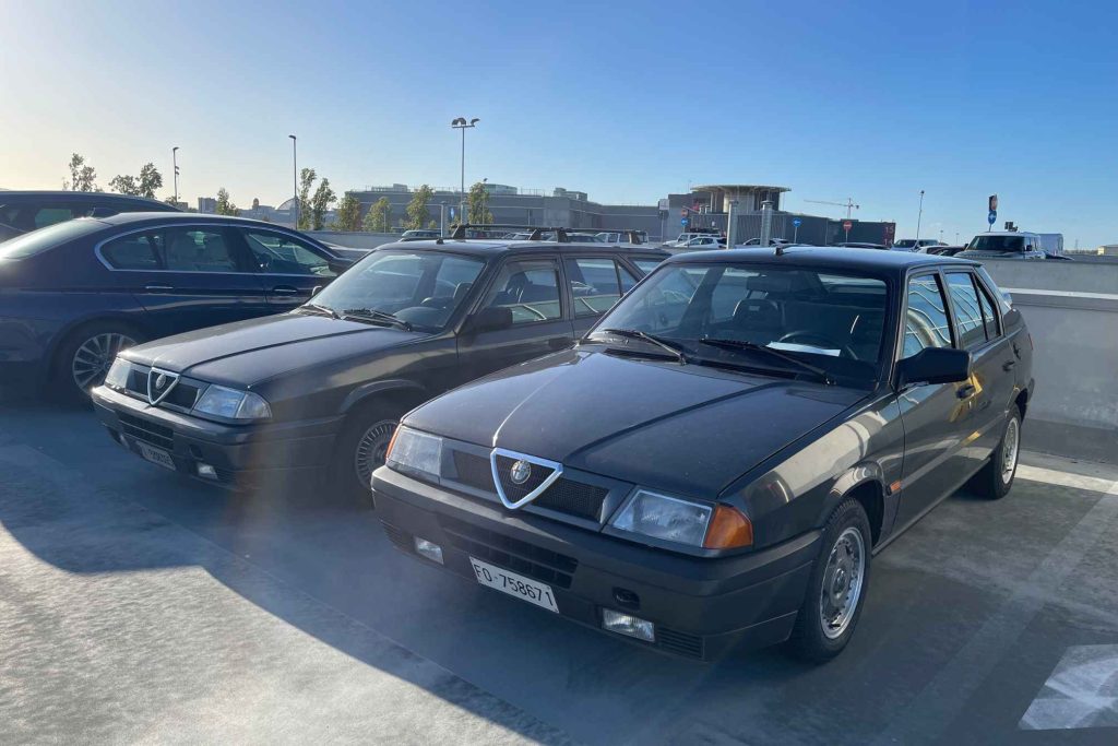 Two black Alfa Romeo sedans parked side by side in a sunny outdoor car park.