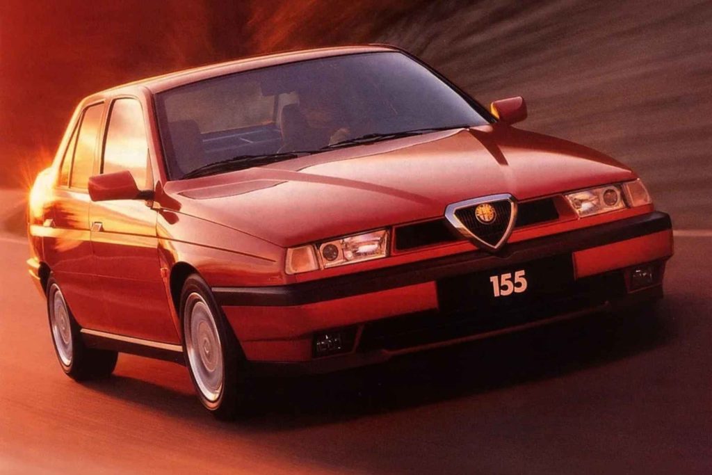 A red Alfa Romeo 155 sedan photographed in motion against a warm red-toned background, showing the front three-quarter view with the distinctive Alfa Romeo shield grille badge and "155" badging on the lower bumper.
