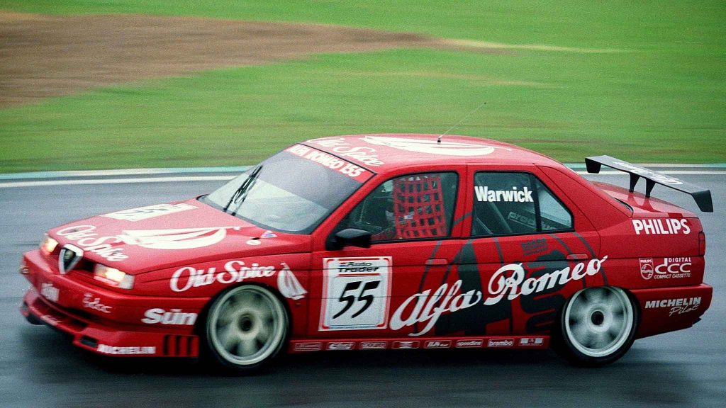 An Alfa Romeo 155 BTCC race car (#55) in Old Spice/Alfa Romeo livery driven by Warwick, captured at speed on a wet circuit with a large rear wing and Michelin/Philips sponsorship.