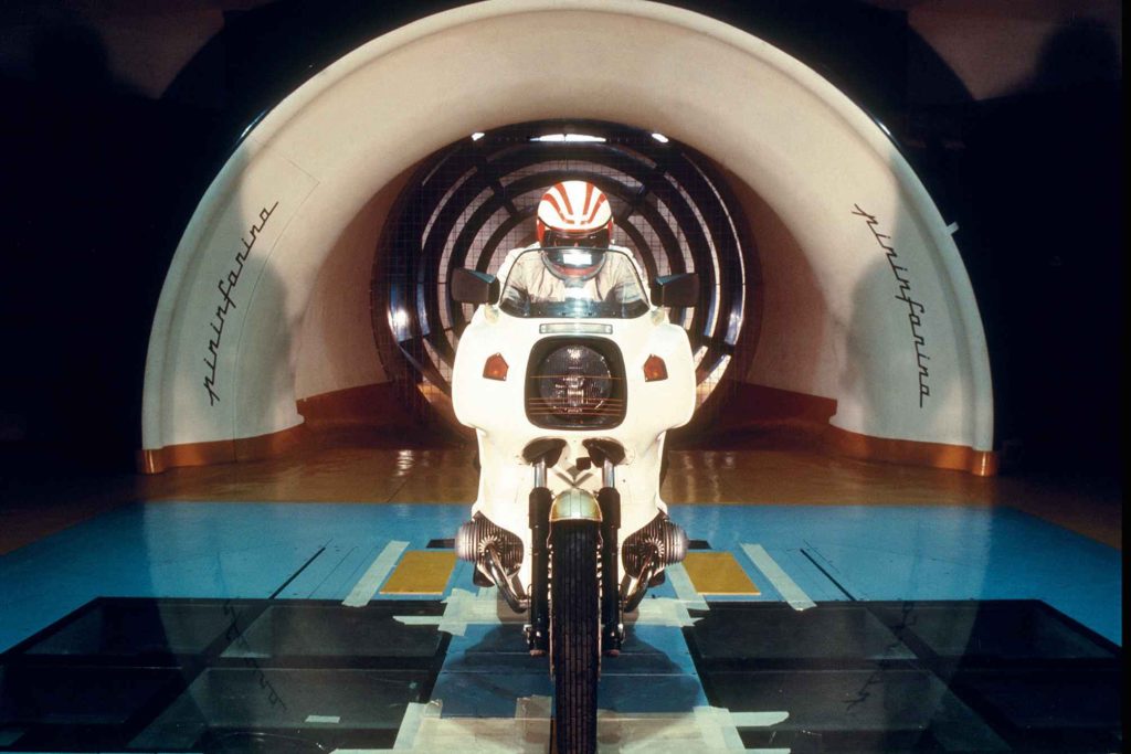 BMW R100RS wind tunnel development shot, front-on view inside the Pininfarina tunnel, rider in white leathers and red helmet behind the full fairing