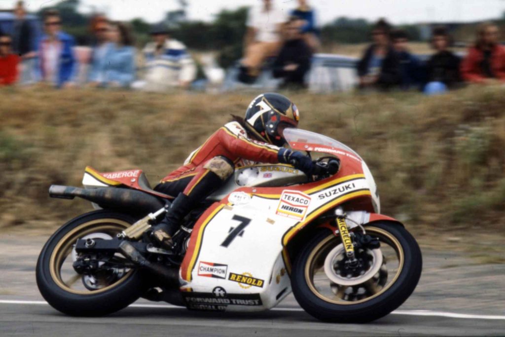 Barry Sheene flat out on his number 7 Suzuki, full-fairing racing crouch, Texaco Heron sponsorship prominent, crowd visible in the background