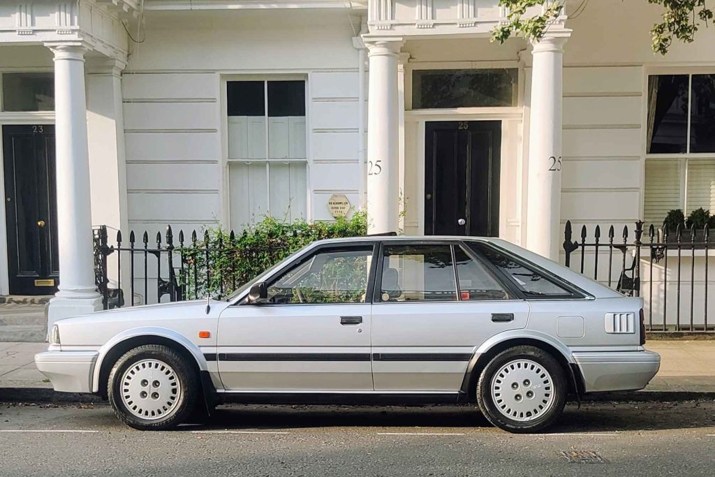 Clean side profile of the silver Nissan Bluebird parked on a quiet London street in front of white Georgian stucco townhouses.