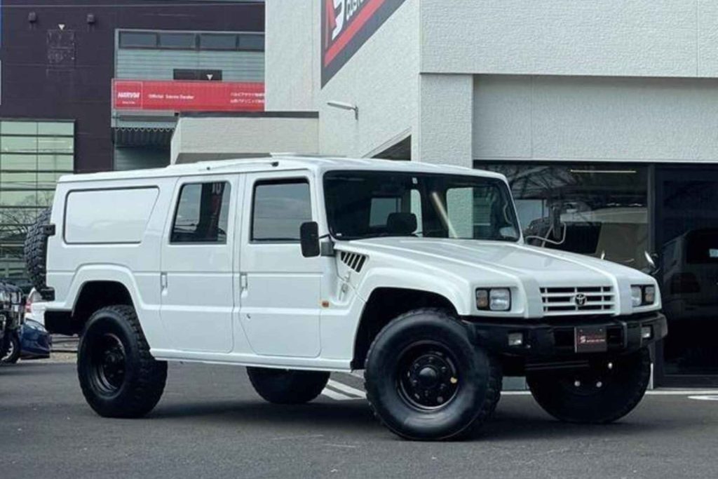 A Toyota Mega Cruiser in white with heavy-duty all-terrain tyres, photographed outside a specialist dealership