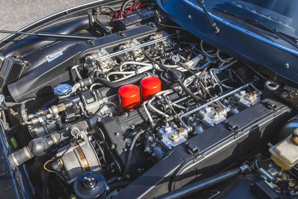 Ferrari 365 GTC/4 engine bay showing the twin-cam V12 engine with six Weber carburetors, red oil filler caps, and extensive ancillary plumbing