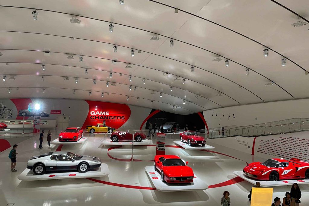 A wide-angle view of the Ferrari Museum's "Game Changers" exhibition hall, showing multiple iconic Ferraris including an F40, 288 GTO, and BB512.
