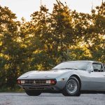 Silver Ferrari 365 GTC/4 at sunset in a three-quarter front pose, set against autumn foliage with wire wheels and classic Italian GT proportions