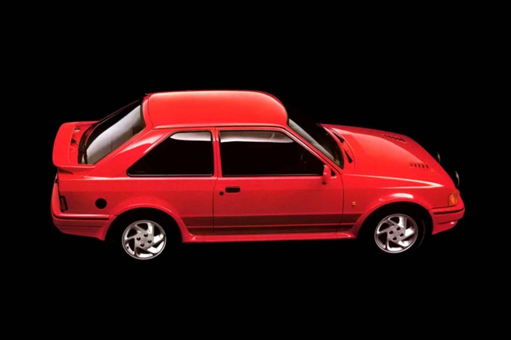 A red Ford Escort RS Turbo in a pure side profile view against a black background, highlighting the fastback roofline, rear spoiler, side skirts, and five-spoke alloy wheels.