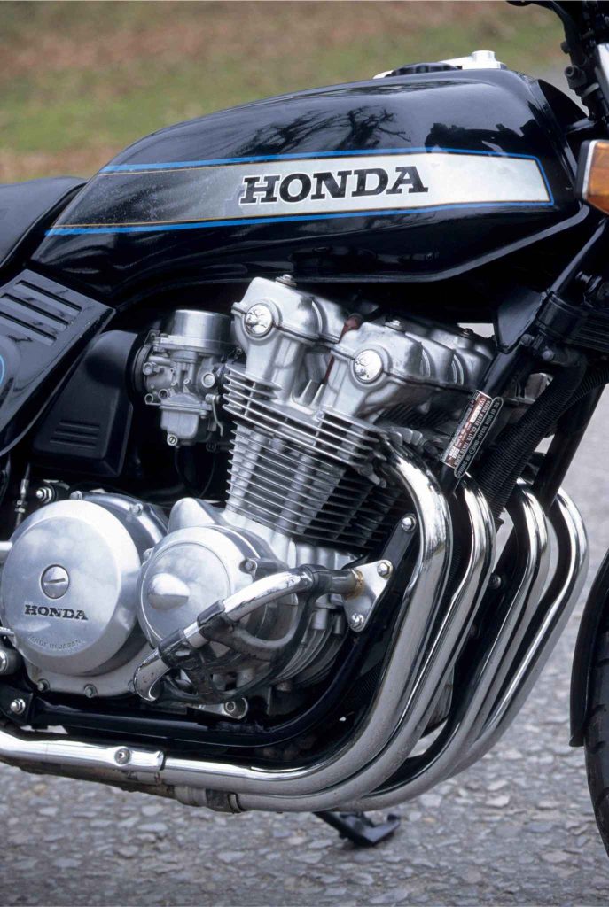 Close-up of the Honda CB900F's 901cc inline-four engine from the left side, showing the carburetors, finned cylinder block, chrome exhaust headers