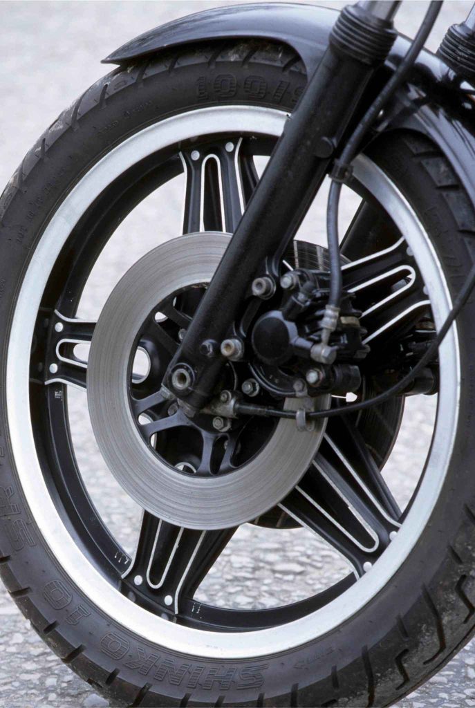 Close-up of the Honda CB900F's front wheel, featuring a distinctive black ComStar cast wheel with machined silver highlights, a single hydraulic disc brake, and telescopic fork leg.