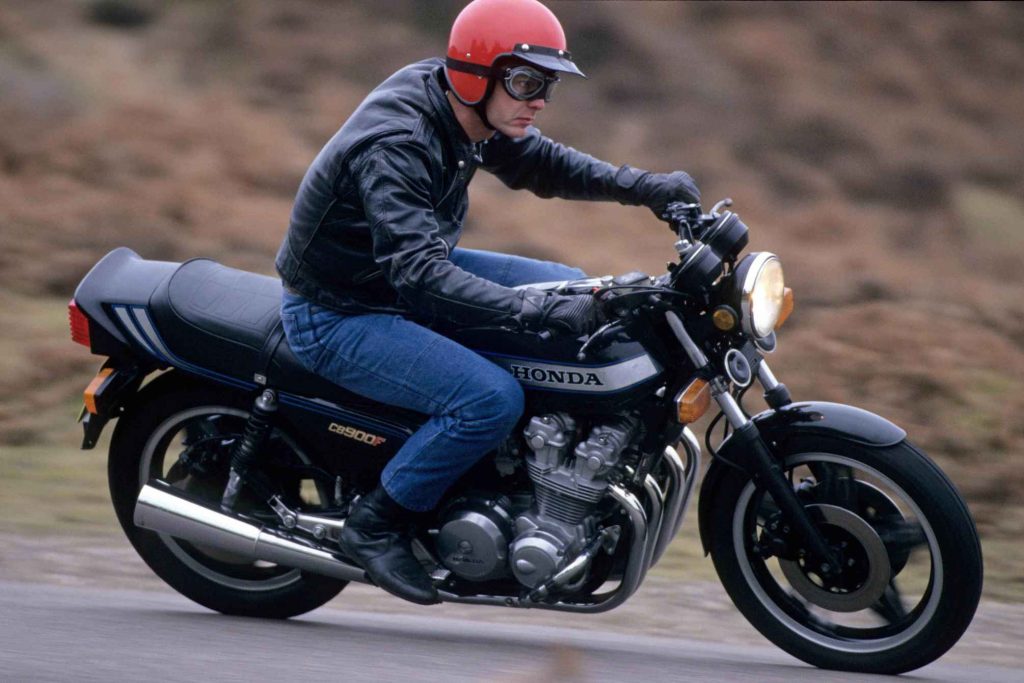 Close three-quarter front view of a rider on a Honda CB900F in motion, showing the CB900F side cover badge clearly, rider leaning slightly forward in riding position.