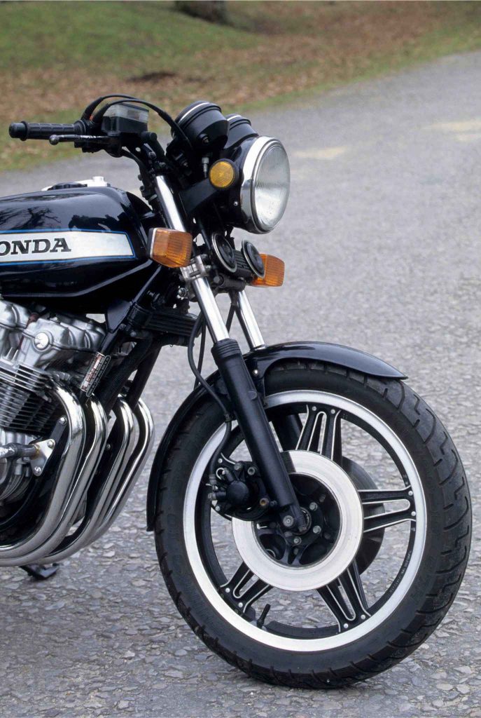 Front three-quarter static shot of the Honda CB900F highlighting the round headlight flanked by amber turn signals, chrome fork legs, black ComStar front wheel, and the four exhaust headers curving downward.