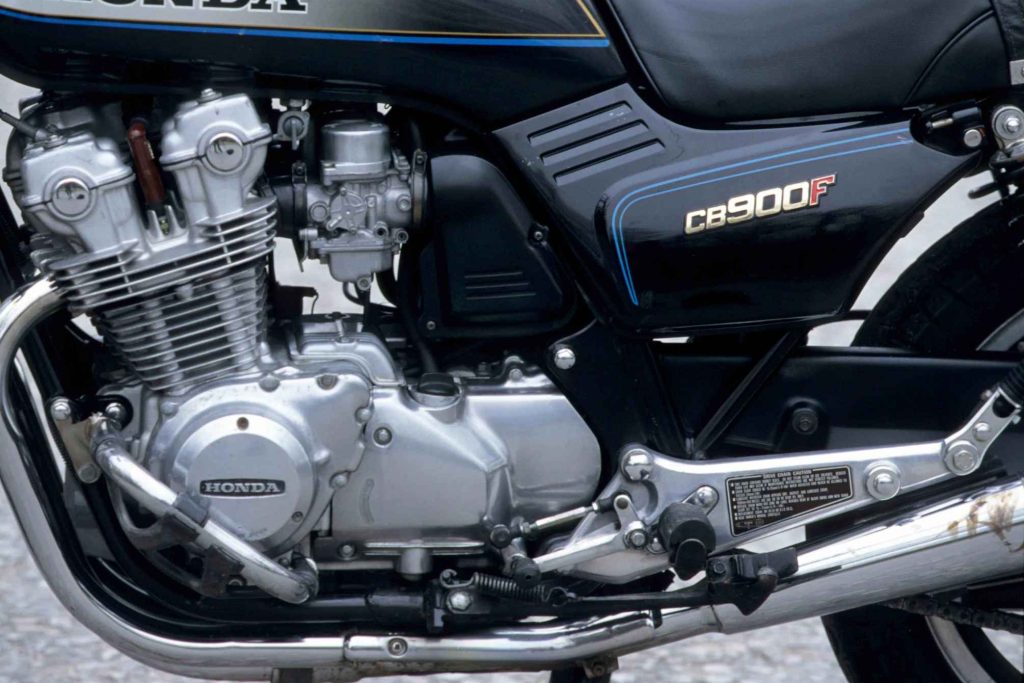 Close-up detail of the Honda CB900F's inline-four engine and upper frame area, showing carburetors, finned cylinder head, and the CB900F side panel badge with blue pinstripe graphics.