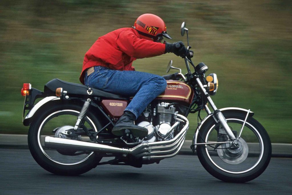 Honda CB400F Super Sport in action, ridden by a rider in a red jacket, showing the four-into-one exhaust system and characterful inline-four engine