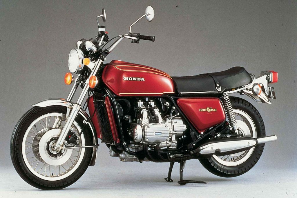 Honda GL1000 Gold Wing studio shot in burgundy red, showing the flat-four liquid-cooled engine, large fuel tank and Gold Wing badging on a grey background