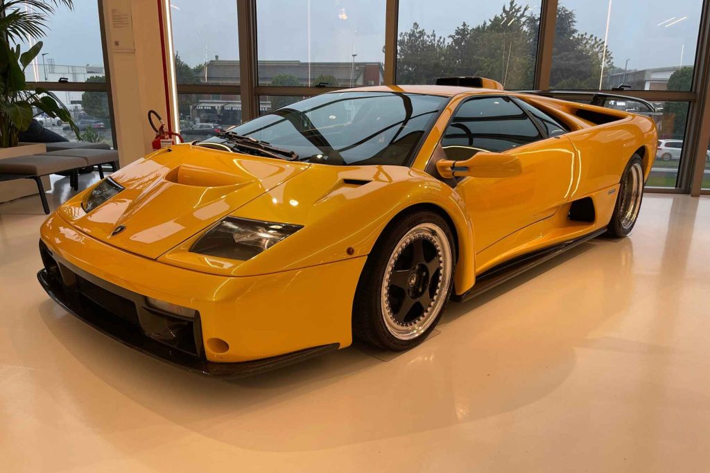 A yellow Lamborghini Diablo GT displayed in a dealership showroom, viewed from the front three-quarter angle.