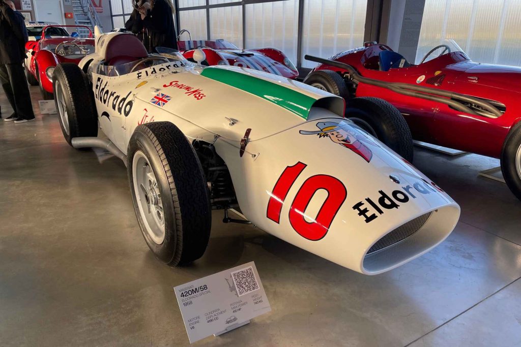 The white Maserati 420M/58 "Eldorado Special" Indy racer displayed in the Maserati Museum alongside red sports-racing cars.