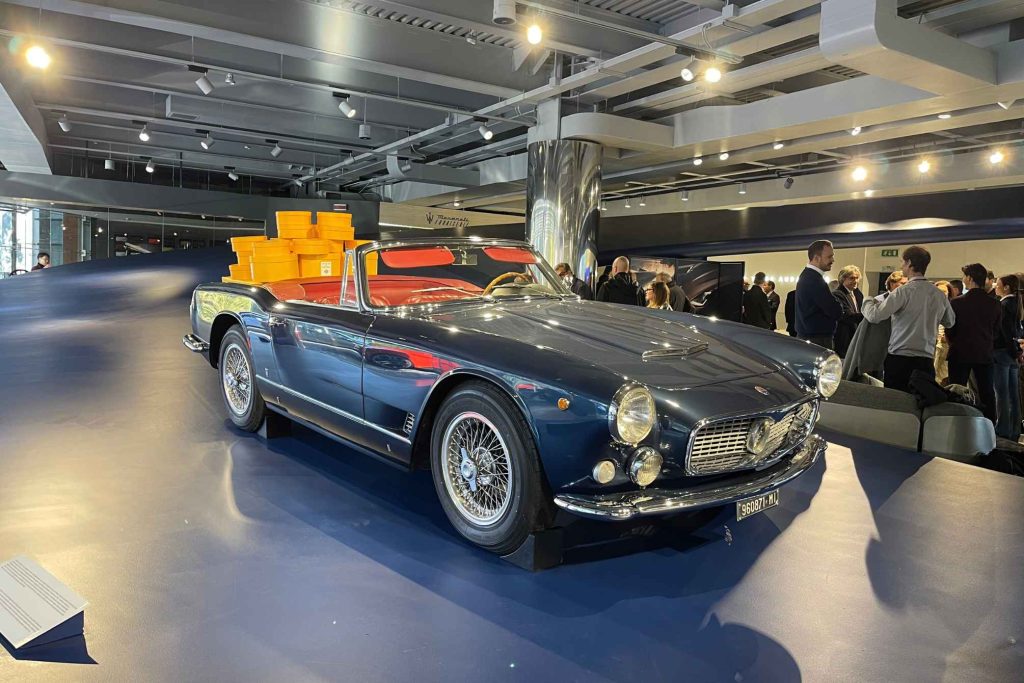 A dark blue Maserati 3500 GT Spyder convertible with red interior and displayed at a crowded Maserati Fuoriserie event with spectators in the background.