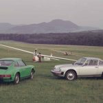 Green and silver Porsche 911 coupes parked on a grass airfield beside a glider, 1970s