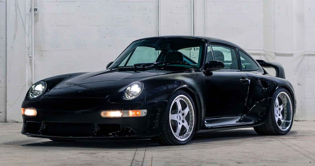 Front three-quarter view of the same gloss black Ruf CTR2 Sport with parking lights illuminated, highlighting the 993-generation round headlights, aggressive front splitter, flared wheel arches, and polished RUF five-spoke wheels.