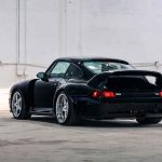 Three-quarter studio shot of the black Ruf CTR2 Sport, emphasising the wide rear haunches, rear wing profile, glowing red tail lights, and polished wheel rims against the bright white background.