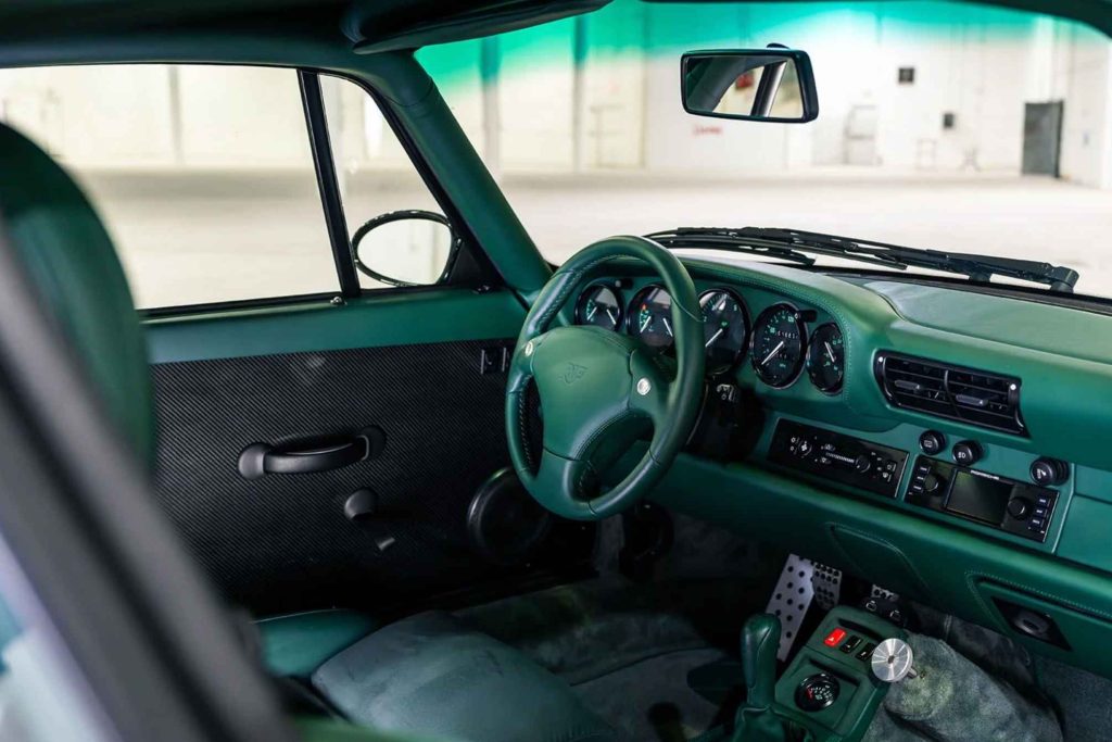 Interior of the Ruf CTR2 Sport showing a full bespoke dark green leather cabin, including the green-stitched Porsche steering wheel with crest, matching green dashboard and door cards with carbon fibre inserts, five-gauge instrument cluster, and aluminium pedals.
